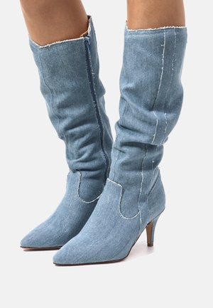 Botines de mezclilla con punta afilada y un diseño aflojado, que cuentan con un cierre de cremallera azul y detalles de costura ligeros, sobre un tacón medio.