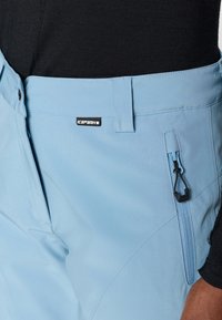 Helle blaue Outdoor-Hosen mit glatter Textur, ausgestattet mit einer Reißverschlusstasche, einem Knopfverschluss und einem "ICEPEAK"-Label am Bund.