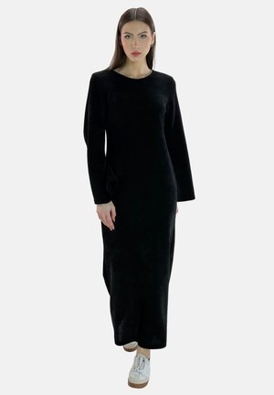 Vestido negro de manga larga hecho de material suave, con un diseño simple y un corte hasta el tobillo, combinado con zapatillas blancas de plataforma.