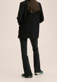 Blazer noir, jeans évasés foncés et baskets turquoise. Le blazer présente un design simple; les jeans sont en denim; les baskets ont un look sportif.