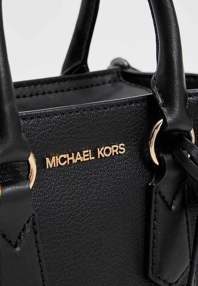 Sac à main en cuir noir avec quincaillerie dorée et marque embossée. Dispose de deux poignées et d'un design structuré avec des coutures visibles.