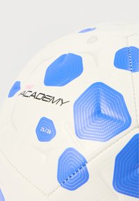 Λευκή ποδοσφαιρική μπάλα με μπλε εξαγωνικά σχέδια, με μαύρο κείμενο "NIKE ACADEMY" και ετικέτα "25/26", κατασκευασμένη από υλικό σύνθετης υφής.