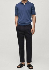 Short-sleeve, navy polo shirt made of knit fabric. Paired with dark trousers and black slide sandals. Simple design with no patterns.