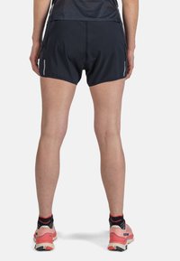 Shorts sportivi neri in un tessuto leggero e liscio. Presentano dettagli riflettenti sui lati e una lunghezza media fino alla coscia. Indossati con scarpe da corsa rosa.