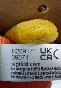 Product label with text in black on a white fabric strip, featuring a yellow textured accent and brown background. Includes branding details.