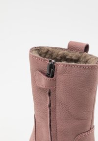 Rosa Leder-Stiefelette mit strukturiertem Finish, ausgestattet mit einem seitlichen Reißverschluss und einem weichen, fellähnlichen Futter an der Oberkante. Dekorative Nähte vorhanden.