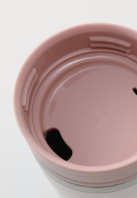 Ceramic tumbler with a pink lid and a black opening. Smooth texture with a circular shape and subtle branding on the inside.