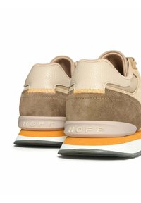 Zapatillas beige y marrón fabricadas en cuero y ante, con un acento naranja, una entresuela blanca y la marca "HOFF" en el talón.