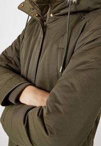 Olijfgroene pufferjack met ritssluiting, gevoerde capuchon van fleece, goudkleurige hardware en gebreide manchetten; voorzien van een borstzak.