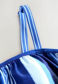 Débardeur à rayures bleues avec bretelles réglables, présentant un design de tissu froncé et une texture lisse. Le dégradé de couleurs comprend différentes nuances de bleu.