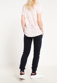 Ljusrosa t-shirt med ett fläckigt mönster, ihop med mörkblåa sweatpants, bärt med vita sneakers. Mjuk tyg med en avslappnad passform.