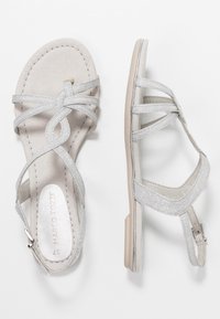 Hopeasandaalit, joissa on nauhat ja litteä pohja, sisältäen mokka-pohjan ja kimaltavia nauhoja, jotka risteävät koristeellista muotoilua varten.