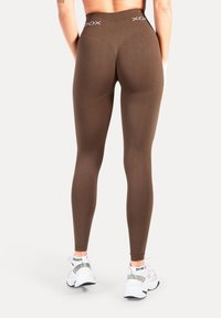 Leggings marrones de cintura alta con una textura suave y logo en la cintura, combinados con zapatillas blancas con detalles reflectantes.