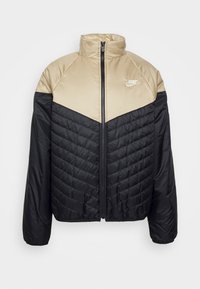 Chaqueta acolchada con parte superior beige y parte inferior texturizada en negro, con cuello alto, cierre de cremallera y un pequeño logo blanco en el pecho.