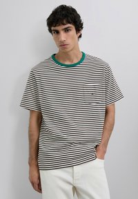 Camiseta de rayas en marrón y blanco, con cuello verde y un bolsillo en el pecho. Está hecha de una tela suave, presenta mangas cortas y un corte recto.