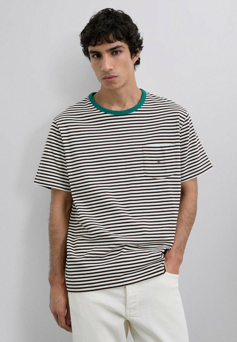 Camiseta de rayas en marrón y blanco, con cuello verde y un bolsillo en el pecho. Está hecha de una tela suave, presenta mangas cortas y un corte recto.