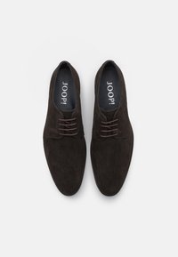 Zapatos de ante marrón oscuro con un acabado suave, punta redondeada y cordones finos. El interior muestra la marca "JOOP!" en la plantilla.