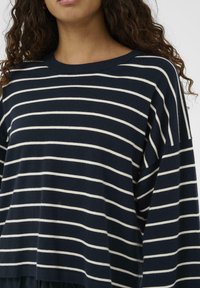 Mørkeblå strikket sweater med hvide vandrette striber, lange ærmer og rund hals; blød tekstur med en afslappet pasform.