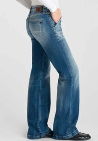 Jean en denim bleu clair évasés avec une apparence délavée, cinq poches et une pièce en cuir marron à l'arrière de la taille.