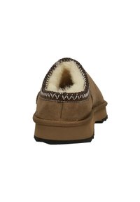 Brun ruskinds slip-on sko med en blød, cremefarvet pelsfoering, afrundet form og kontrastsyede kanter omkring åbningen. Flad gummisål.