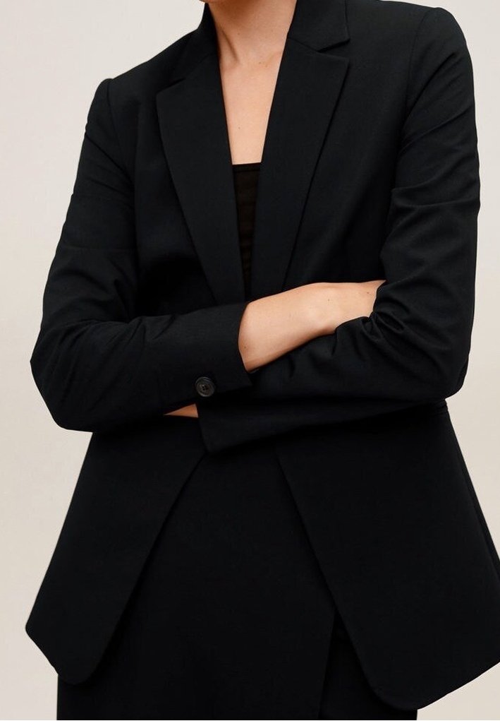Blazer nero su misura con rever a punta, maniche lunghe e dettagli a bottoni. Tessuto liscio con una vestibilità strutturata e tasche laterali.