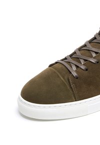 Zapatillas de ante marrón con suela de goma blanca, que cuentan con cordones grises y una punta redondeada, destacando una textura suave y un diseño minimalista.