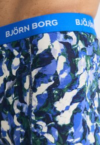 Kék elasztikus derékpánt „BJÖRN BORG” logóval; kék, zöld és fehér mintázattal; puha anyag; testhezálló fazon.