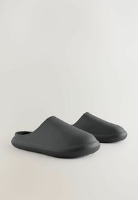 Svarta, slip-on-träskor gjorda av gummi med en slät yta, rund tå och låg sula. Minimalistisk design utan utsmyckningar.