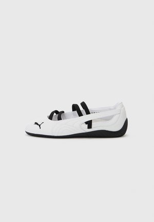 Baltie sporta apavi ar melniem akcentiem, ar noapaļotu purngalu, elastīgām siksnām un teksturētu gumijas zoli. Puma logo priekšpusē.