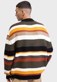 Pull en tricot avec des rayures horizontales vertes, noires, blanches, orange et bordeaux. Présente une texture côtelée et un design de col classique.