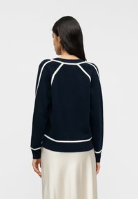 Μπλε ναυτικό πλεκτό πουλόβερ με λευκές λεπτομέρειες· διαθέτει στρογγυλή λαιμόκοψη, μακριά μανίκια και εφαρμοστό τελείωμα. Λεπτή υφή, casual σχεδίαση.