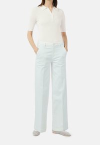 Biała, prążkowana koszulka polo z krótkim rękawem w połączeniu z jasnoniebieskimi spodniami o szerokim kroju, z zapięciem na guziki z przodu i bocznymi kieszeniami.
