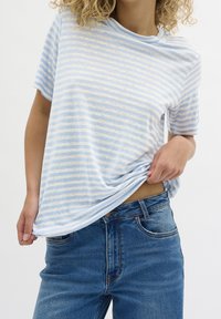 Camiseta de manga corta a rayas en azul claro y blanco, hecha de una tela suave, combinada con unos pantalones vaqueros de tiro alto en azul, con una textura ligeramente arrugada.