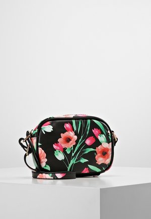 Zwarte crossbodytas met roze en rode bloemenprint en verstelbare band, geplaatst op een wit voetstuk tegen een grijze achtergrond.