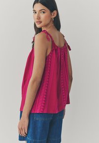 Fuchsia ärmelloses Top mit strukturiertem Muster, ausgestattet mit verstellbaren Bindebändern und Raffung am Ausschnitt.