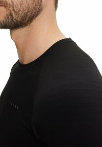 Zwarte sportshirt van gladde stof, met gestructureerde strepen op de schouders en een vlakke halslijn. Logo verschijnt nabij de onderkant.