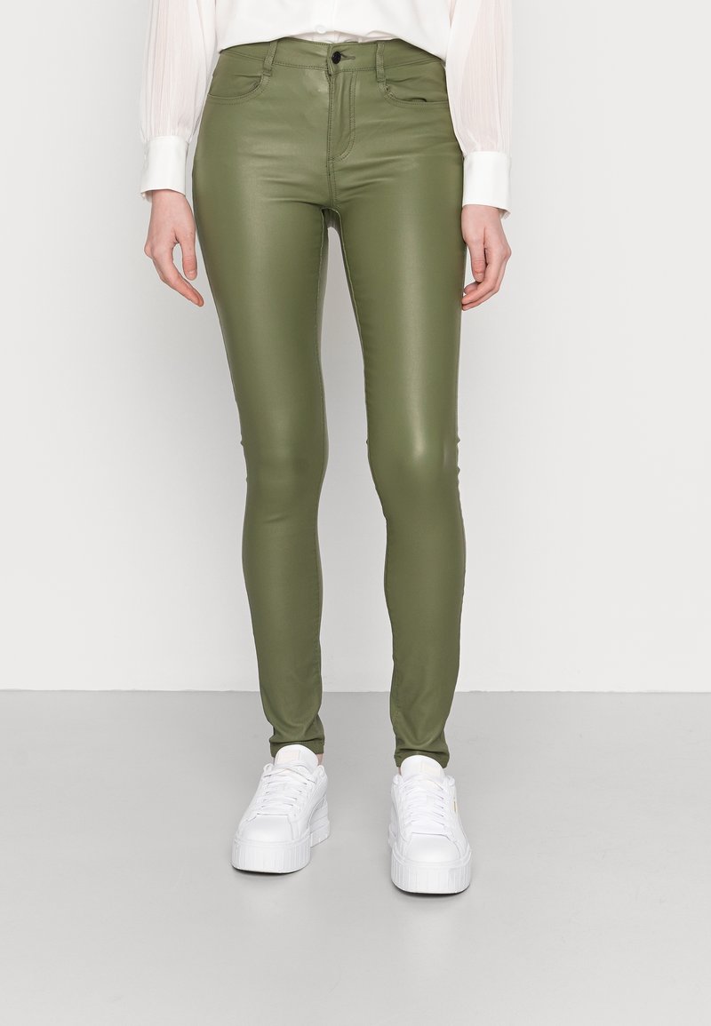 Zelené syntetické kožené skinny kalhoty s lesklým povrchem, doplněné bílými chunky teniskami. Obsahují pět kapes a mají vysoký pas.