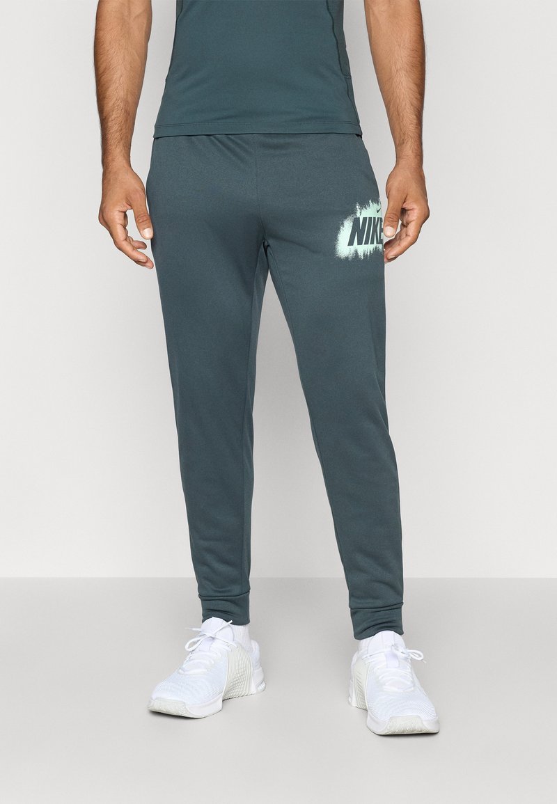 Dresy Nike w ciemnym odcieniu teal, wykonane z miękkiego materiału. Posiadają elastyczny pas, slim fit oraz biały akcent z logo na lewym udzie.