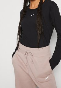 Svart långärmad tröja med en vit Nike-logga, ihop med ljusrosa sweatpants som har dragsko i midjan och sidofickor.