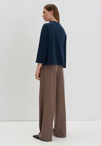Navy blue cropped sweatshirt with wide three-quarter sleeves paired with brown high-waisted wide-leg pants. Smooth fabric, minimal design.