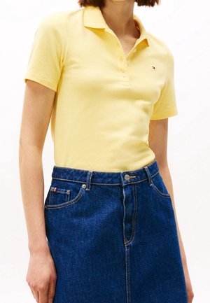 Gul bomulds polo shirt med krave, parret med en høj talje denimnederdel med frontlukning og mørkeblå farve.