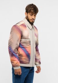 Padded jacket in soft beige with colorful abstract patterns in orange, purple, and blue. Features a front zipper and classic collar.
