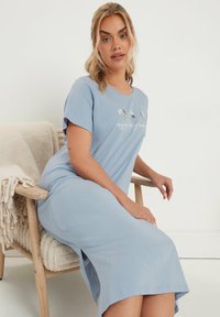 Vaaleansininen puuvillayöpyjama lyhyillä hihoilla, jossa on kukkakirjontaa ja sivuhalkio mukavuutta varten, neutraalilla taustalla.