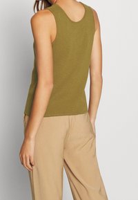 Olivgrünes, tailliertes Tanktop mit rundem Ausschnitt und sichtbaren Nähten. Leichter, dehnbarer Stoff, kombiniert mit beige, locker sitzenden Hosen.