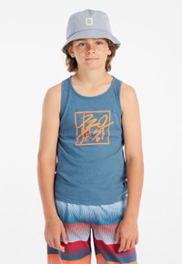 Blauwe tanktop met oranje grafisch ontwerp aan de voorkant, gecombineerd met multicolour gestreepte zwembroek. Lichtblauwe emmerhoed. Gladde stof.