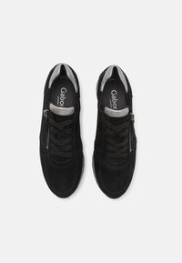 Black suede sneakers with laces and a side zipper, featuring a silver rim around the opening. Brand logo visible inside.