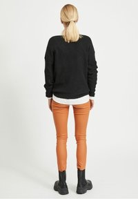 Czarny sweter dzianinowy o luźnym kroju, zestawiony z dopasowanymi pomarańczowymi skórzanymi spodniami i czarnymi botkami za kostkę. Widoczna plain biała koszula pod spodem.