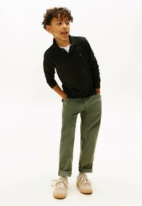 Sort langærmet polotrøje kombineret med olivengrønne chinos og beige sneakers. Trøjen har en krave og et diskret logodetalje.