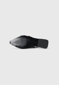 Black flat shoe with a pointed toe, textured surface, and minimalistic design. Features a discreet emblem and smooth heel.