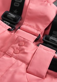 Rosa vattentät bib med en slät textur, med justerbara svarta remmar med en logo, två matchande knappar och sydda detaljer.